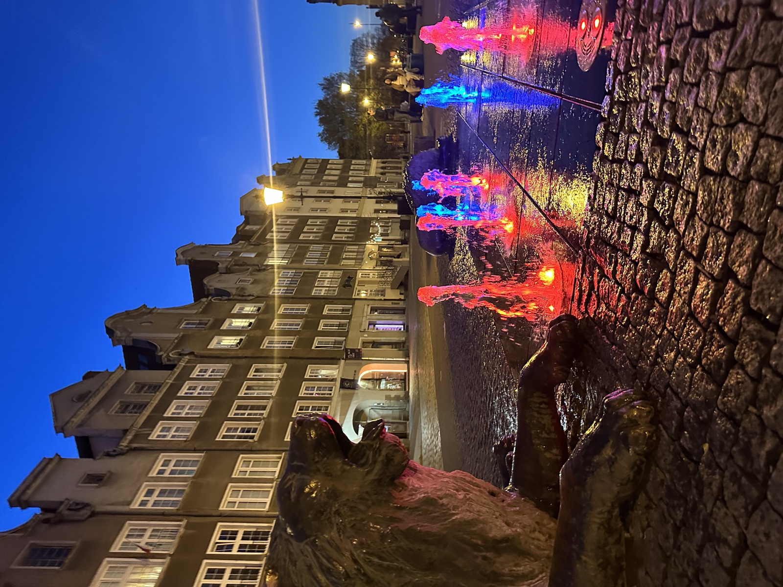A fountain illuminated at night with red and blue light in the water, Hanseatic gables behind